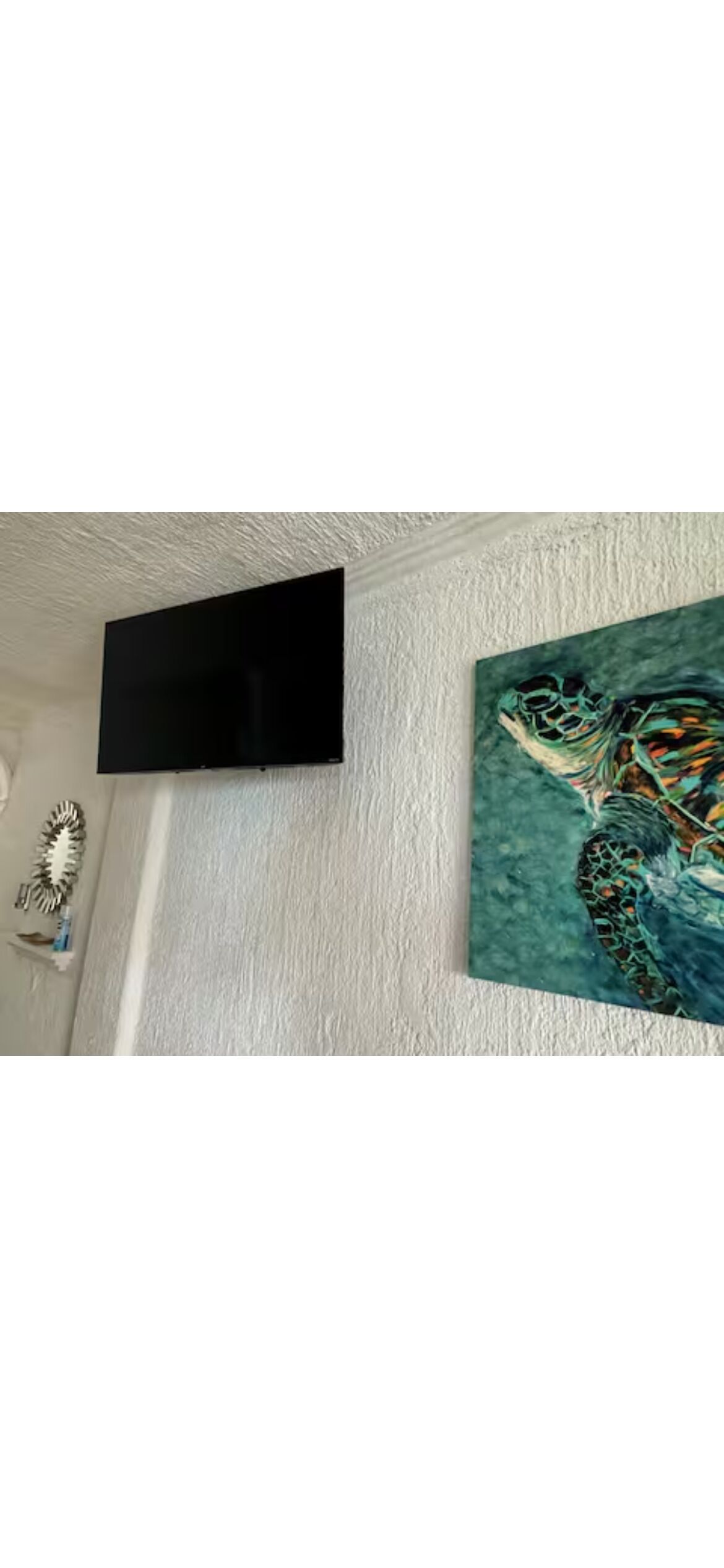 Une pièce dotée d’un téléviseur à écran plat fixé au mur, d’un tableau aux motifs abstraits et d’un miroir décoratif.