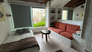 Ein gemütliches Wohnzimmer mit einem roten Sofa, einem kleinen runden Tisch und einem Bett mit einer braunen Decke.
