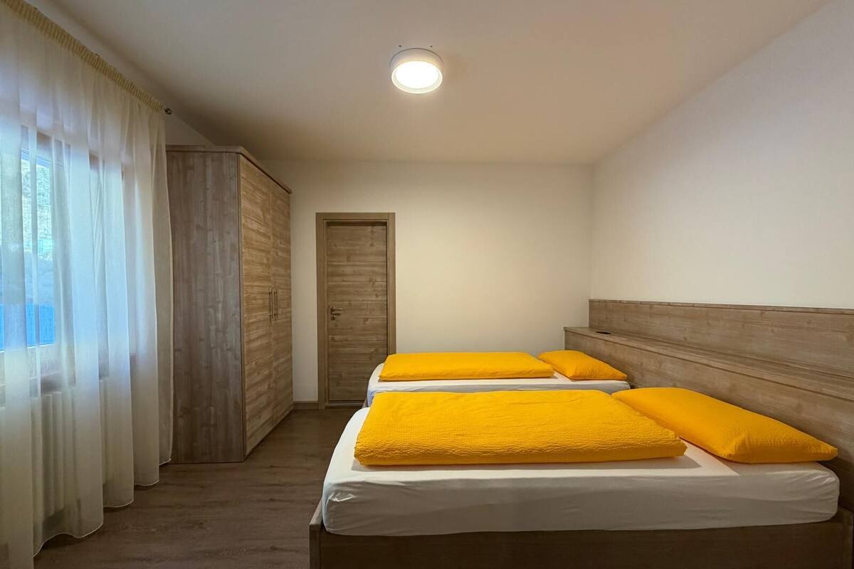 A room with two beds, each with yellow pillows, a wooden wardrobe, and a door.