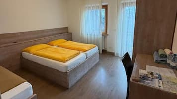 Quarto com duas camas, uma escrivaninha, uma cadeira e uma janela com cortinas.