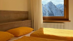 Un dormitorio con cabecera de madera, un ventanal con vistas a la montaña y una cama con ropa de cama amarilla.