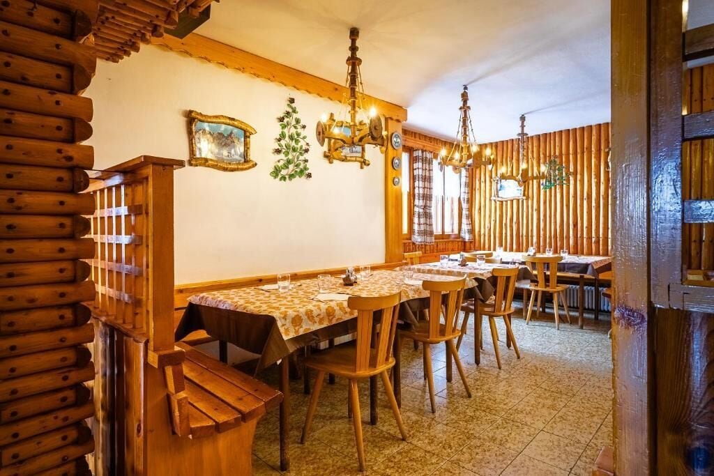 A dining area with wooden walls and tables, a chandelier, and a wooden bench.