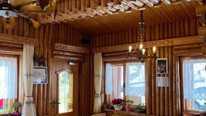 Un interior rústico de madera con varias mesas y sillas, un candelabro y amplias ventanas con cortinas.