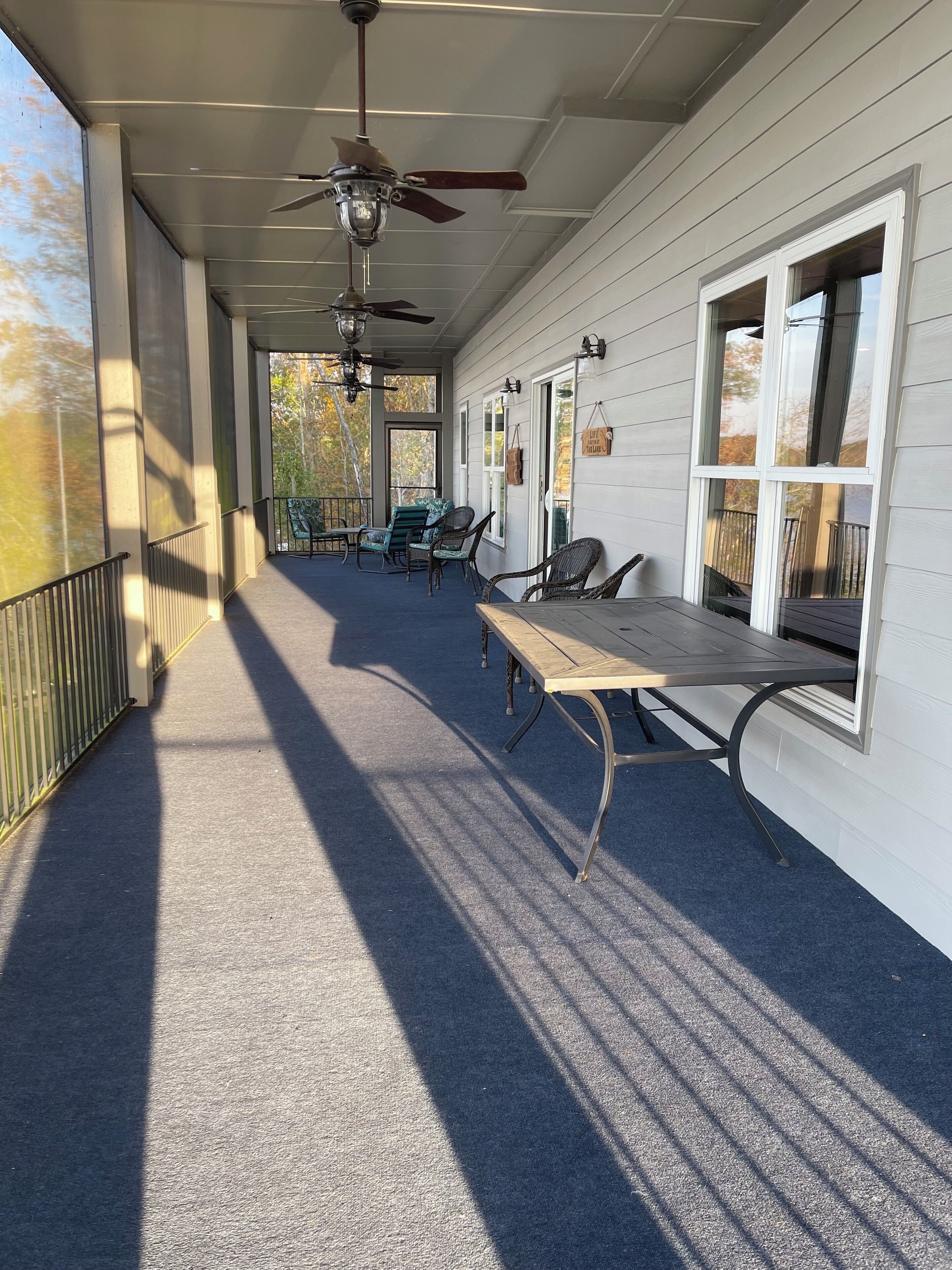 Eine überdachte Veranda mit Tisch und Stühlen, einem Deckenventilator und Fenstern mit Leuchten.