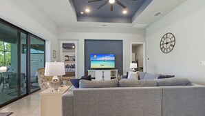 A modern living room with a grey sectional sofa, a flat-screen TV, and a ceiling fan. - Cape Luxe Canal Retreat - Saltwater Pool & Game Room & Kayaks (Cape Coral)