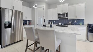 A modern kitchen with white cabinets, stainless steel appliances, a marble island, and pendant lighting. - Cape Luxe Canal Retreat - Saltwater Pool & Game Room & Kayaks (Cape Coral)