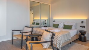 A modern hotel room with a large bed, a seating area with chairs, a small table, and a mirror. - FLH Funchal Studio Blue View Gardens (Funchal)