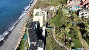 An aerial view of a coastal hotel with a beachside location, solar panels on the roof, and a swimming pool. - FLH Ocean View Escape at Acqua Residences (Funchal)