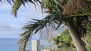 A wooden boardwalk along a coastal path with a metal railing on one side, leading to a view of the sea and a building in the distance. - FLH Ocean View Escape at Acqua Residences (Funchal)