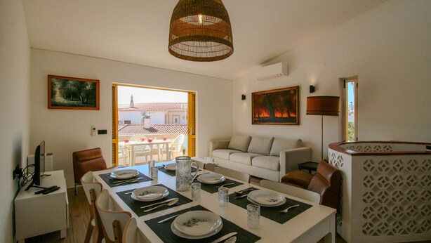 Comedor con una mesa lista para cuatro personas, un sofá blanco y vista a un edificio.