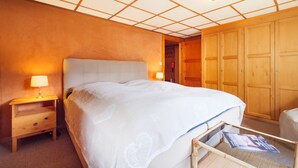 Et hotelværelse med en stor seng, et træskab, sengeborde med lamper og et sofabord i glas med magasiner.