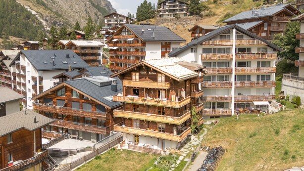 Et fjeldresort med træbygninger, altaner og en skibakke i baggrunden.