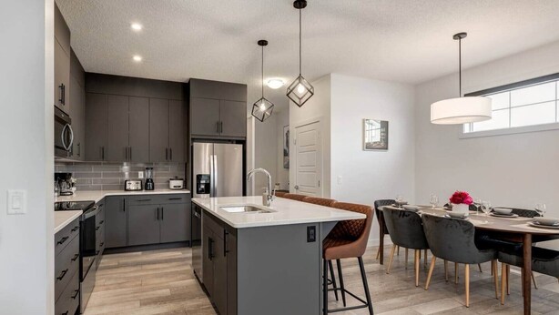 A modern kitchen with grey cabinets, a stainless steel refrigerator, and a central island with stools. - 7-Bedroom Getaway with AC, Hot Tub, BBQ, Garage and Pet-Friendly Amenities (Calgary)