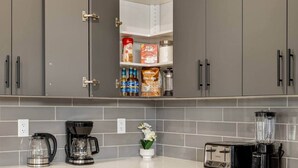 A modern kitchen with grey cabinets, a coffee maker, a toaster, and a blender on the counter. - 7-Bedroom Getaway with AC, Hot Tub, BBQ, Garage and Pet-Friendly Amenities (Calgary)