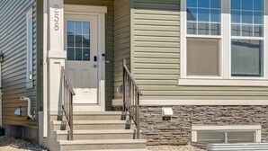 A two-story house with a front porch, a stone foundation, and a mailbox. - 7-Bedroom Getaway with AC, Hot Tub, BBQ, Garage and Pet-Friendly Amenities (Calgary)