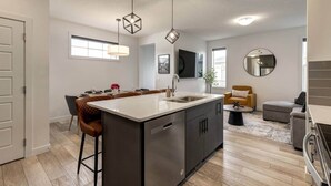 A modern kitchen with a central island, bar stools, and pendant lighting. - 7-Bedroom Getaway with AC, Hot Tub, BBQ, Garage and Pet-Friendly Amenities (Calgary)
