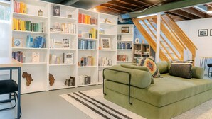 Un racó de lectura acollidor amb un sofà verd, una biblioteca blanca plena de llibres i una escala de fusta.