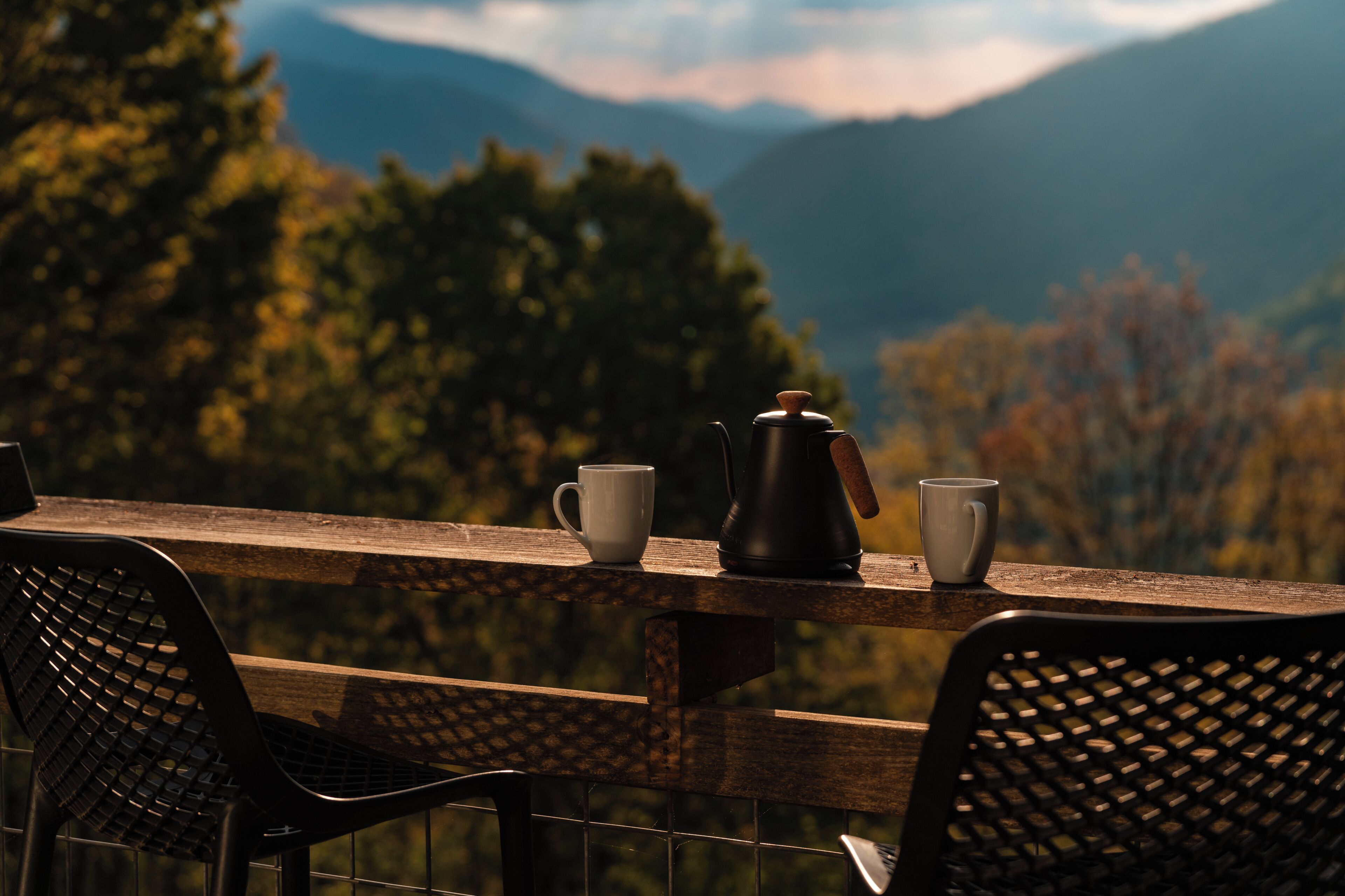 A wooden table with two chairs, a coffee pot, and two cups.