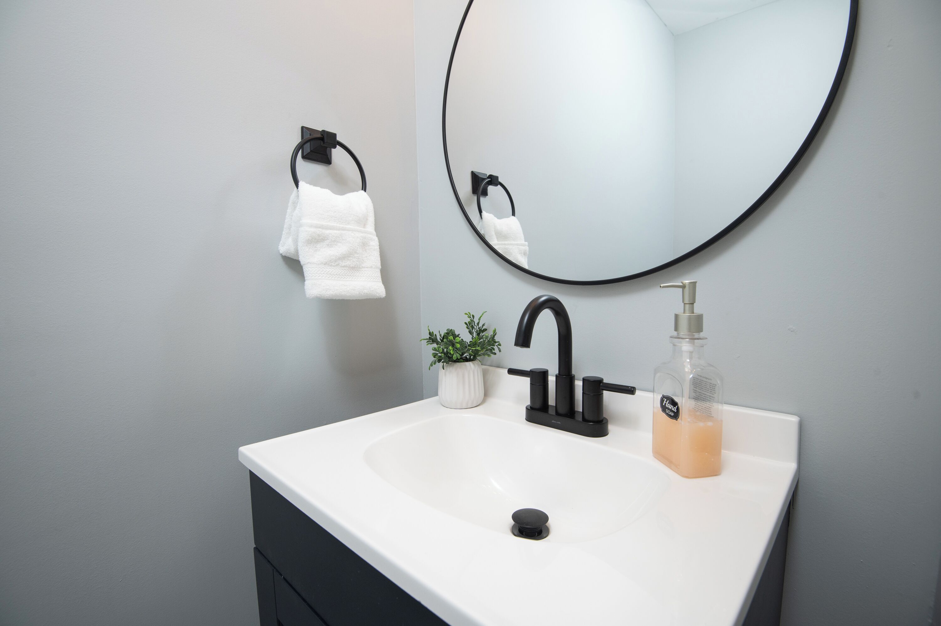 Une salle de bain avec un lavabo blanc, un robinet noir et un miroir rond.