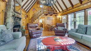 L’intérieur d’une cabane en rondins, avec une cheminée en pierre, des fauteuils en cuir, une table rouge et un escalier en bois.