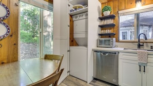 Une cuisine compacte avec un coin repas, des meubles en bois, un lave-vaisselle et une fenêtre donnant sur un espace verdoyant.