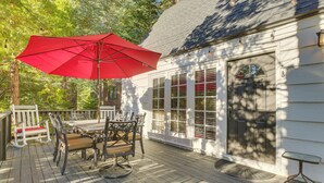 Une terrasse en bois avec une table et des chaises, un parasol rouge et un bâtiment blanc doté de fenêtres.