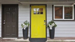Una casa con una puerta principal marrón oscuro y una puerta amarilla brillante, flanqueada por dos macetas con flores blancas.