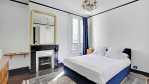 Een slaapkamer met een groot bed, een spiegel, een open haard en een kroonluchter.