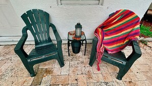 Dos sillas Adirondack verdes, un farol y una manta a rayas coloridas sobre un patio con baldosas.