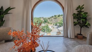 Una habitación con un amplio ventanal arqueado, un sofá, una mesa con una planta y otra planta en maceta junto a la ventana.