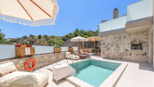 Zona de piscina con sillones de descanso, un flotador salvavidas y un muro de piedra.