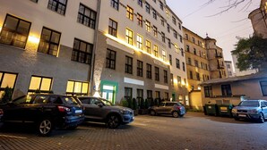 A multi-story hotel with a row of windows on the ground floor, several parked cars, and a brick-paved parking area. - Spacious & Quiet Apt with Terrace 1-BR, Riga Centre (Rīga)