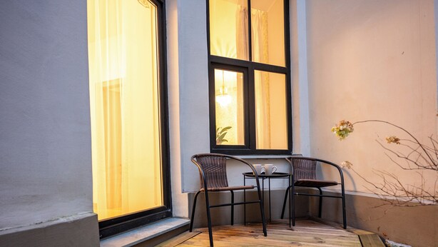 A corner patio with two wicker chairs and a small round table, a window with curtains, and a potted plant on the right. - Spacious & Quiet Apt with Terrace 1-BR, Riga Centre (Rīga)