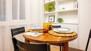 A dining area with a round wooden table set for four, surrounded by black chairs. There are two glass candle holders on the table, and a woven placemat under the plates. A white shelf with decorative items and a framed picture is in the background. - Spacious & Quiet Apt with Terrace 1-BR, Riga Centre (Rīga)
