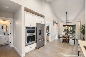 Eine moderne Küche mit eingebauten Geräten, eine Essecke mit Tisch und Stühlen und ein Ausblick ins Freie durch große Fenster.