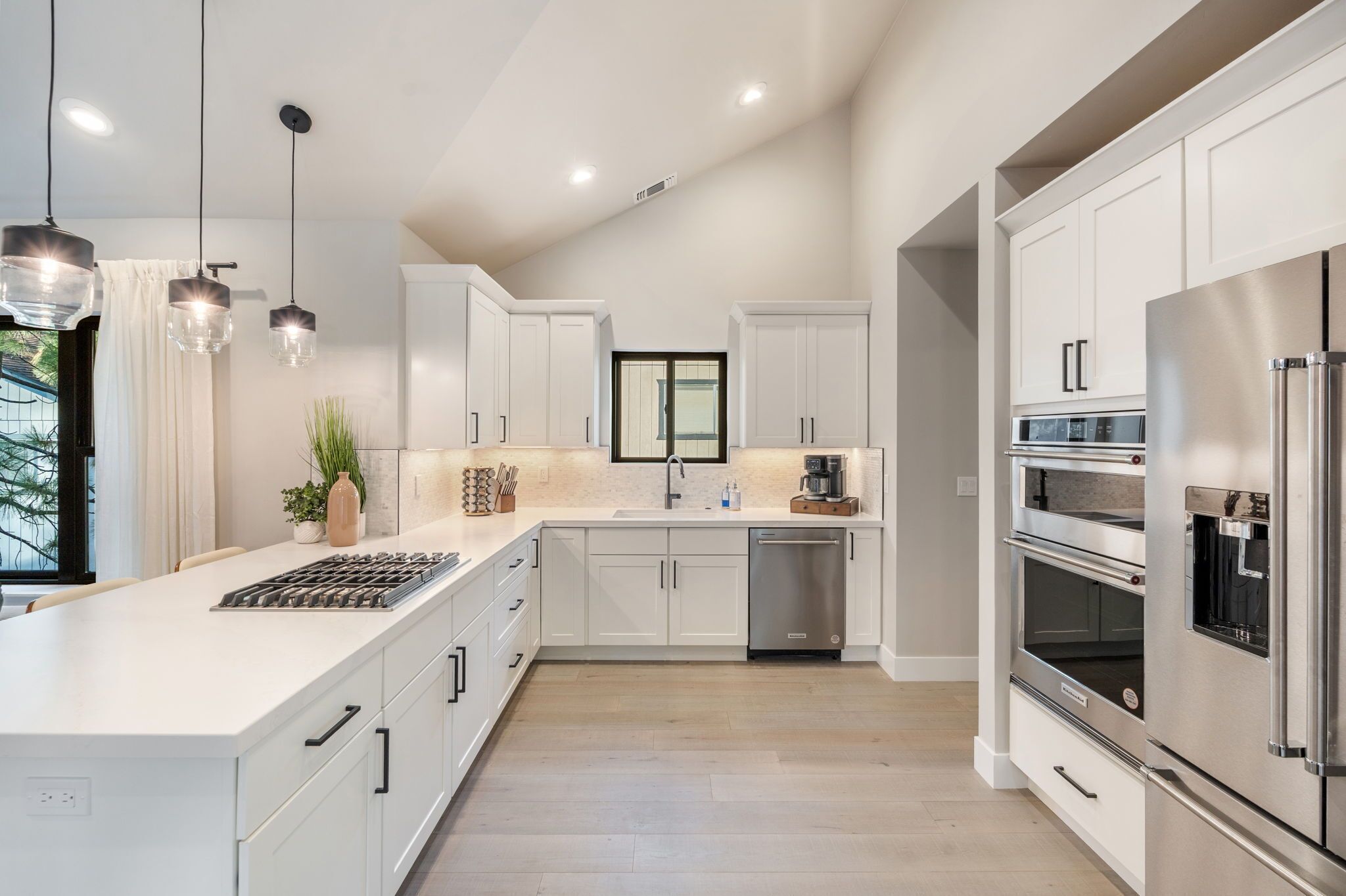Une cuisine moderne avec des meubles blancs, des appareils en acier inoxydable et des luminaires suspendus.