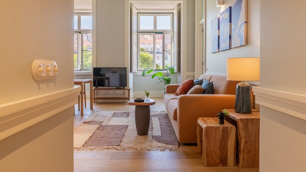 Un salon comprenant un canapé, une table basse, un téléviseur et une fenêtre donnant sur des immeubles.