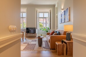 A living room with a sofa, a coffee table, a TV, and a window with a view of buildings. - FLH Heart of Rossio Apartment IV (Lisboa ciudad)