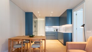 Una cocina moderna con armarios azules, una mesa de comedor de madera con sillas y un sofá en una sala de estar luminosa.