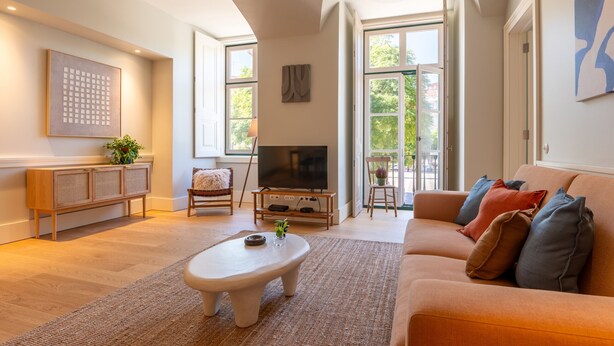 Un salon moderne avec un canapé, une table basse et un téléviseur. On y trouve également des fenêtres, une plante et un meuble.