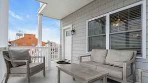 Une véranda avec un banc en bois et un canapé, une petite table et une balustrade blanche.
