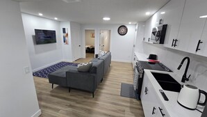 Eine moderne Wohnung mit grauem Sofa, einer Küche mit weißen Schränken und einem Essbereich.