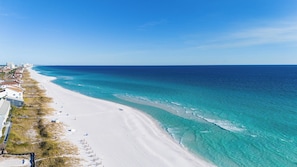 A coastal beach with clear turquoise waters, white sand, and a row of buildings along the shore. - Crystal Sands • 2 Minutes to Beach • Pool & Hot Tub • FREE Golf Cart & Bikes (Destin)