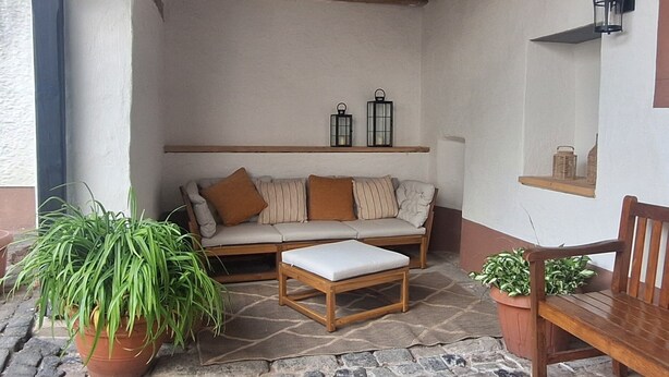 Un espace extérieur aménagé dans un style rustique, avec un sol carrelé en pierre, des meubles en bois et des plantes en pot.