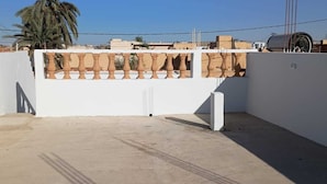Una terraza en la azotea con un muro blanco, una barandilla decorativa y una palmera al fondo.