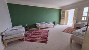 Una habitación con tres camas de madera, una pared verde, un tapete rojo estampado y una puerta blanca.