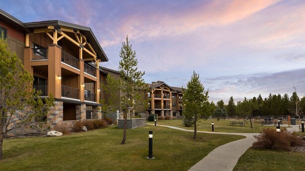 A modern building with a stone facade, multiple balconies, and a well-maintained lawn. - WorldMark West Yellowstone condo with easy access to Yellowstone West Gate. (West Yellowstone)