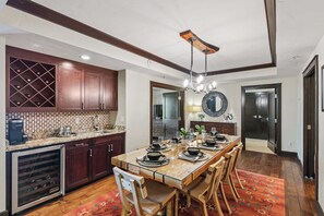 A modern kitchen with dark wood cabinets, a wine cooler, and a dining area with a glass table and wooden chairs. - Three-Bedroom · 2 Bath · Kids Den ·  Sleeps 7 (Truckee)