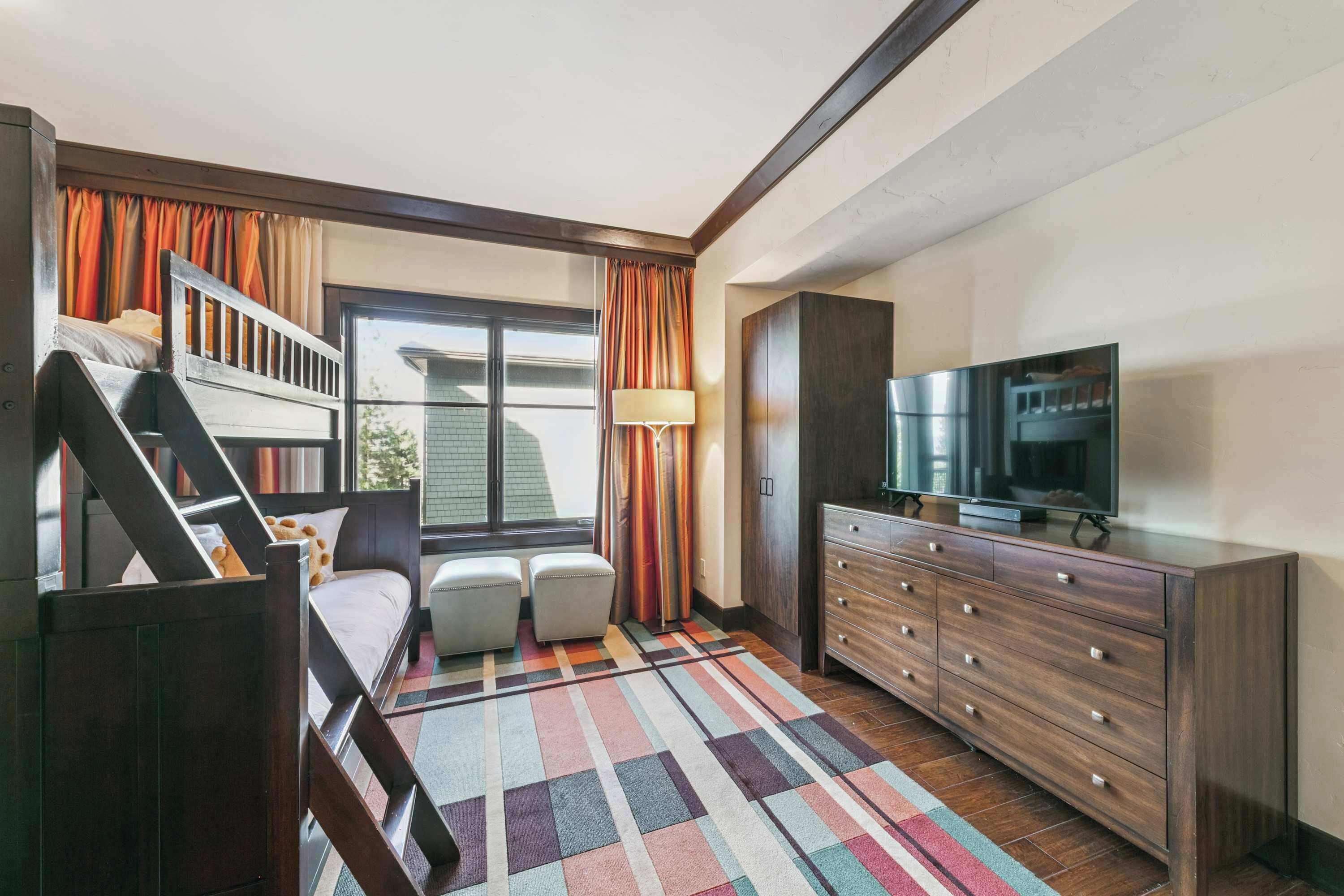 Una habitación con literas, un escritorio, una silla, televisión, cómoda y una ventana con cortinas.