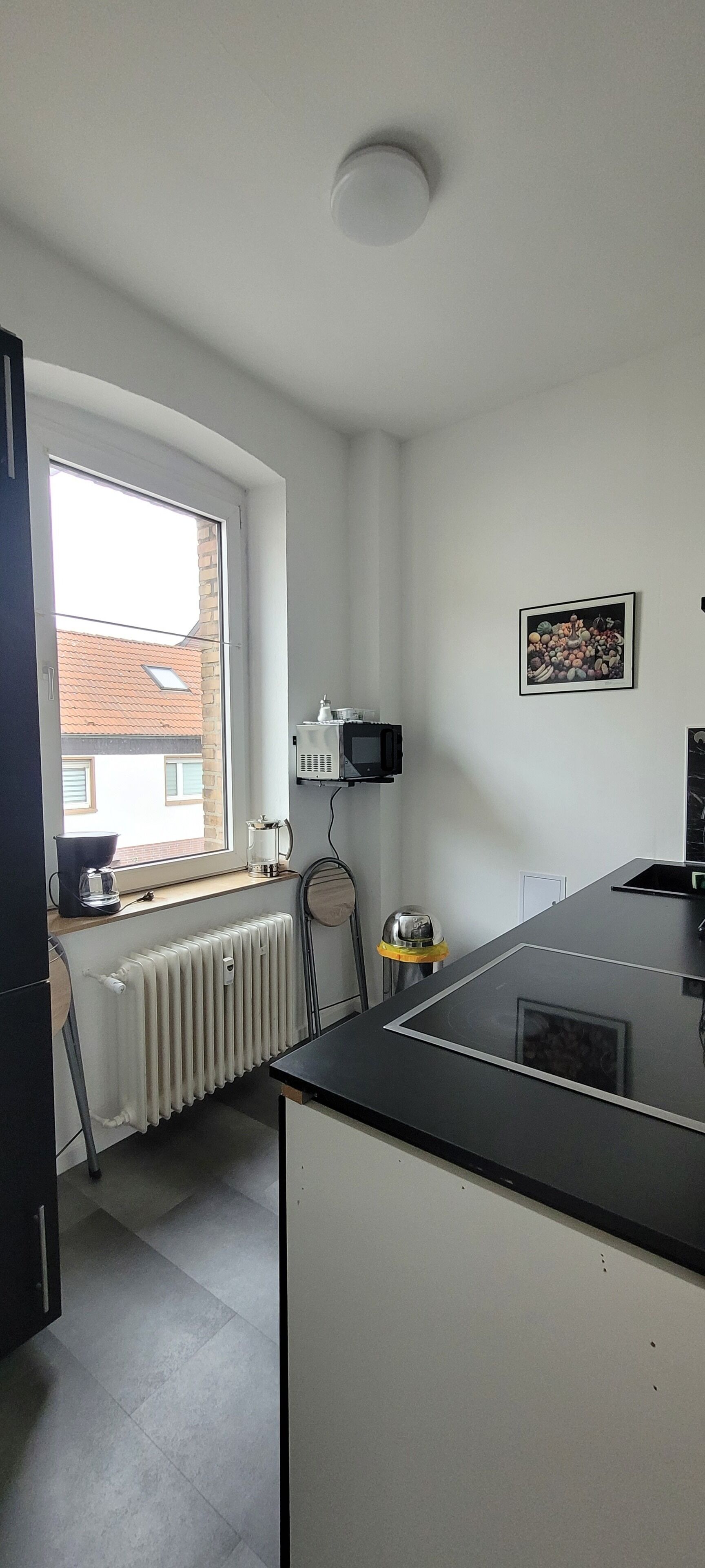 Une cuisine moderne avec une fenêtre, un radiateur, une machine à café et un four à micro-ondes.